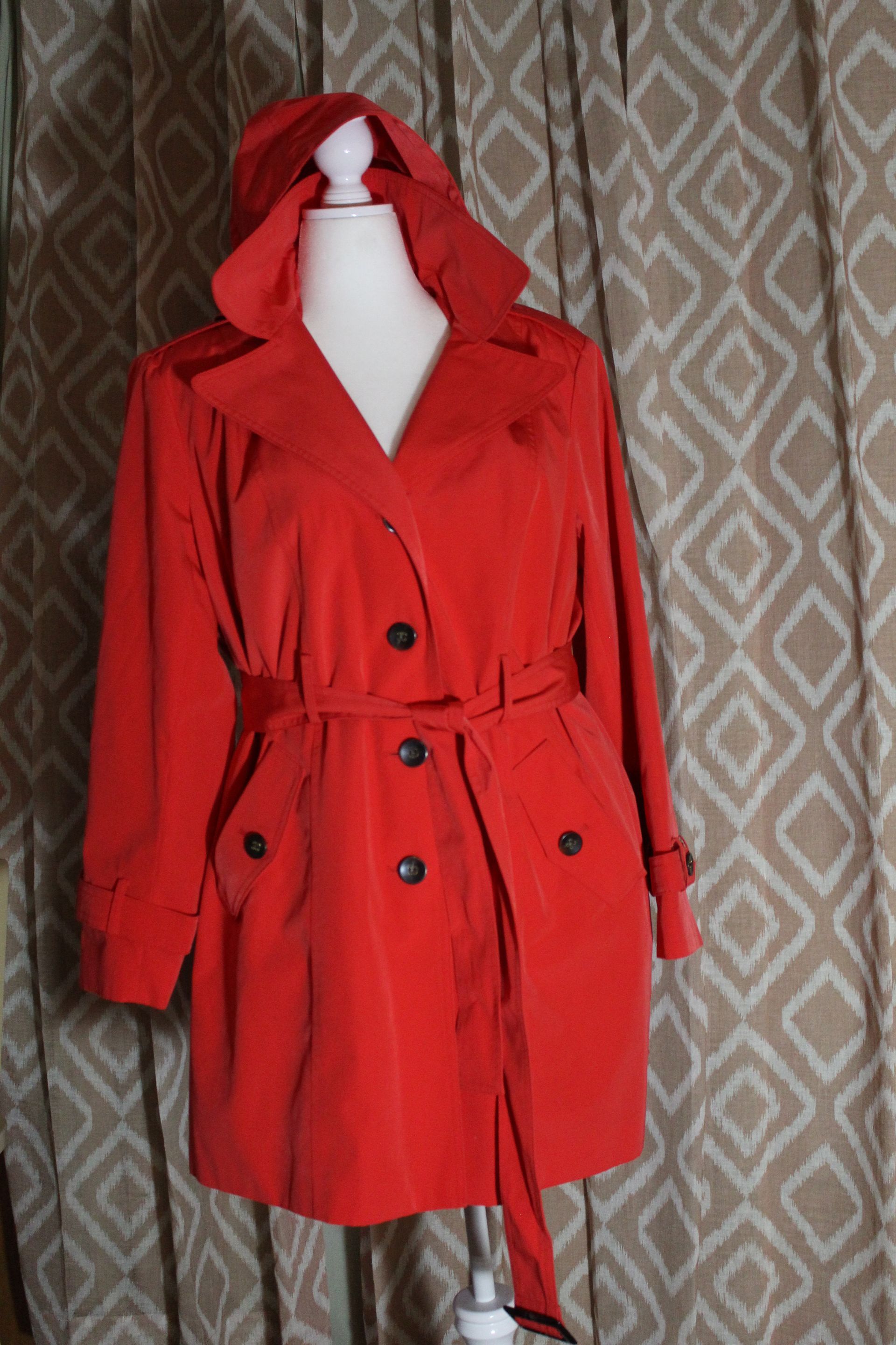 Red hooded trench coat with black buttons on a mannequin against a patterned backdrop