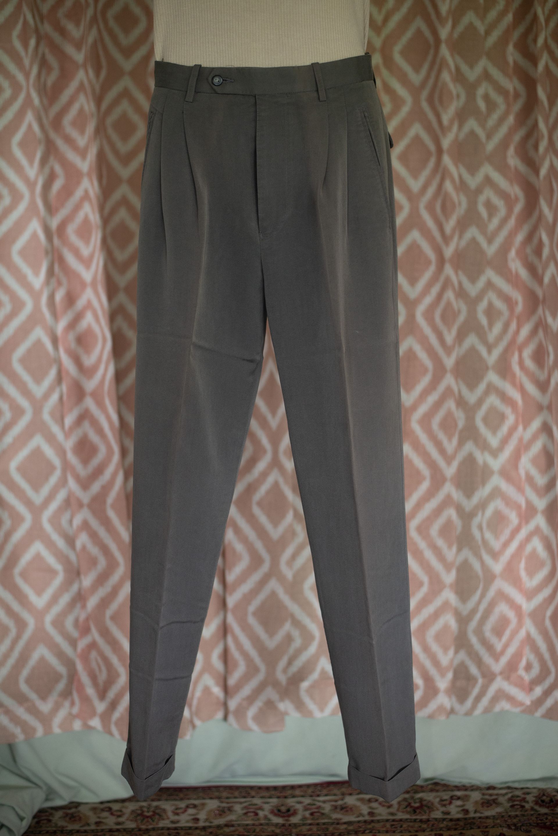 Gray pants hanging against a patterned curtain.