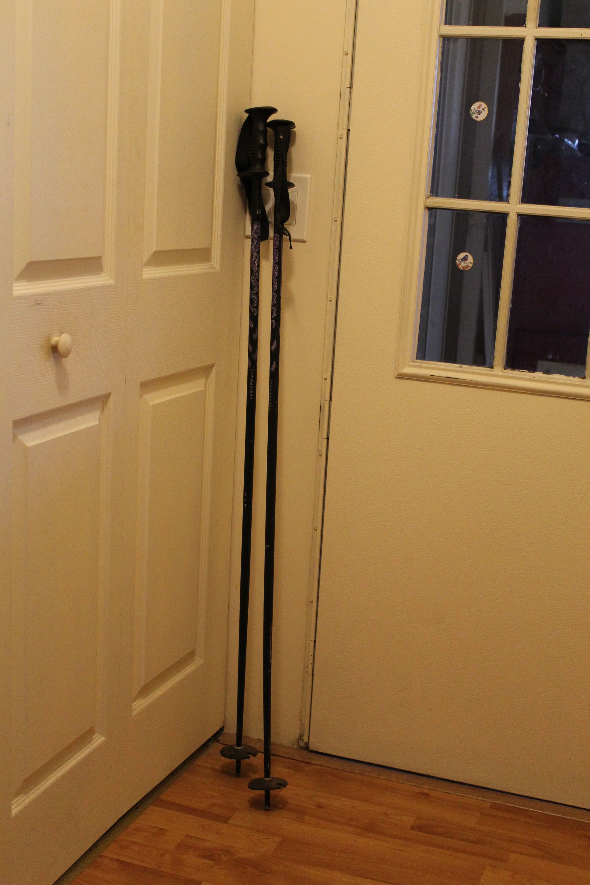 Walking cane stand beside a white door in a small beige room with a window and wood floor