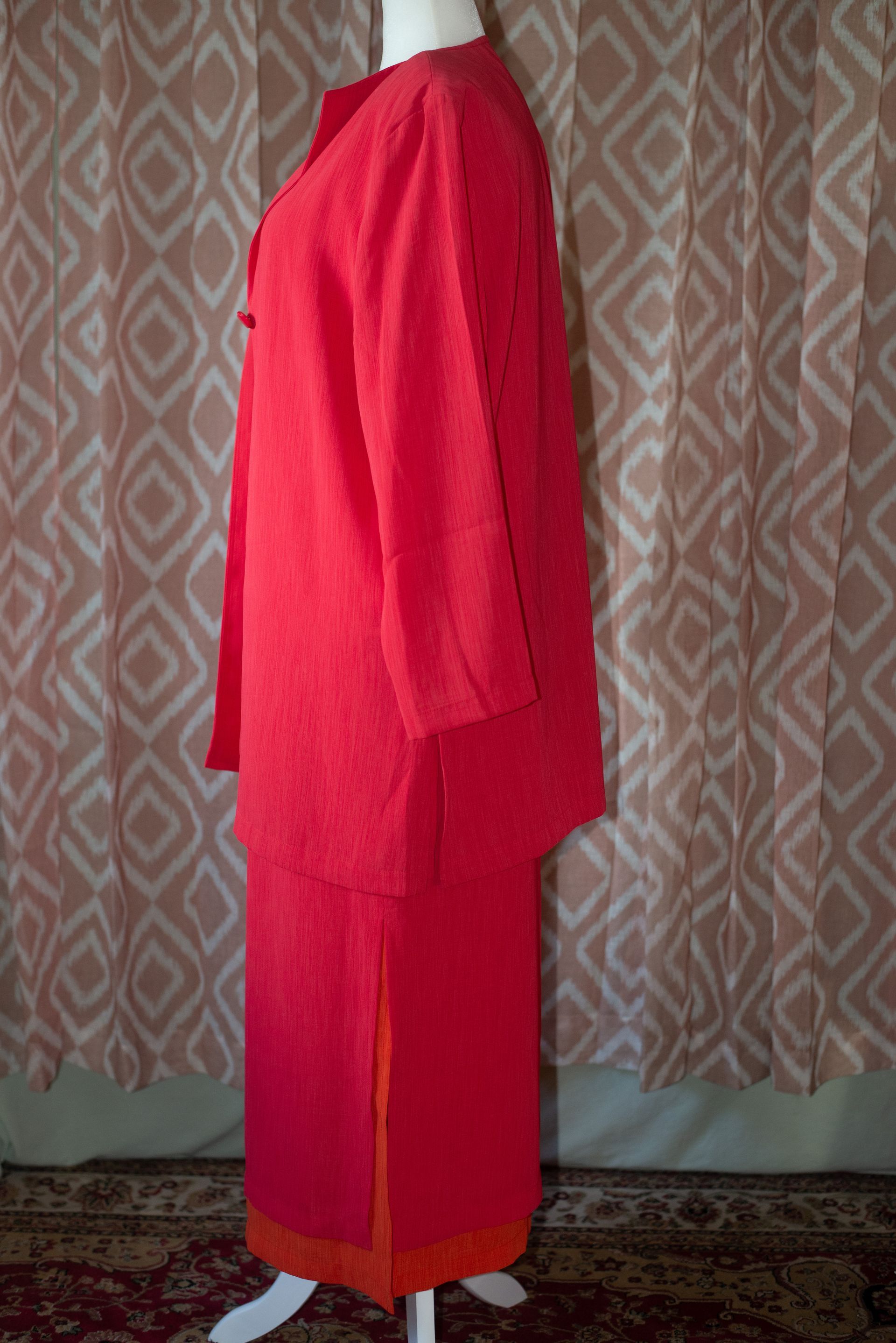 Pink jacket and matching skirt displayed on a mannequin against a patterned backdrop