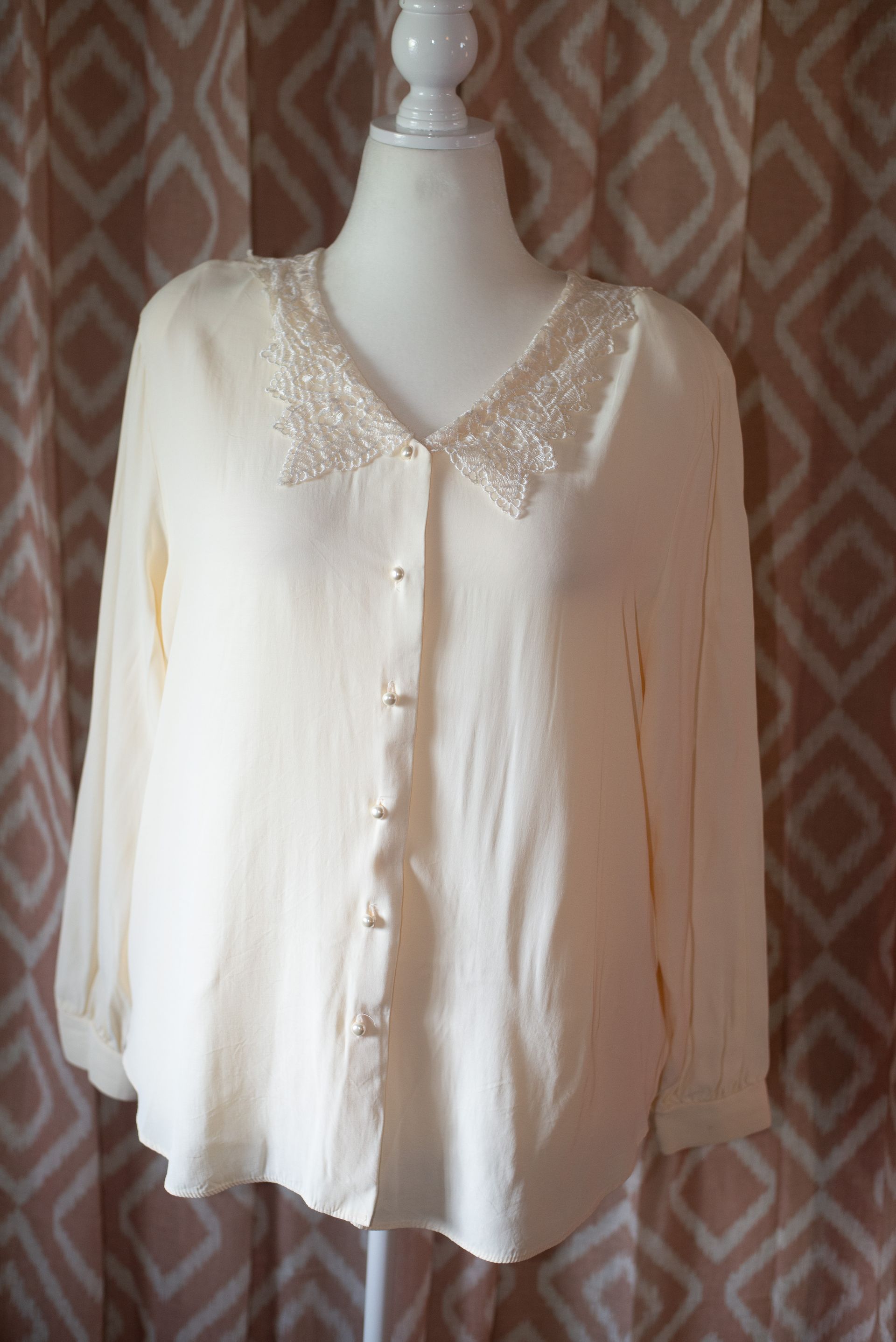 Cream button-up blouse with lace trim on the collar, displayed on a mannequin