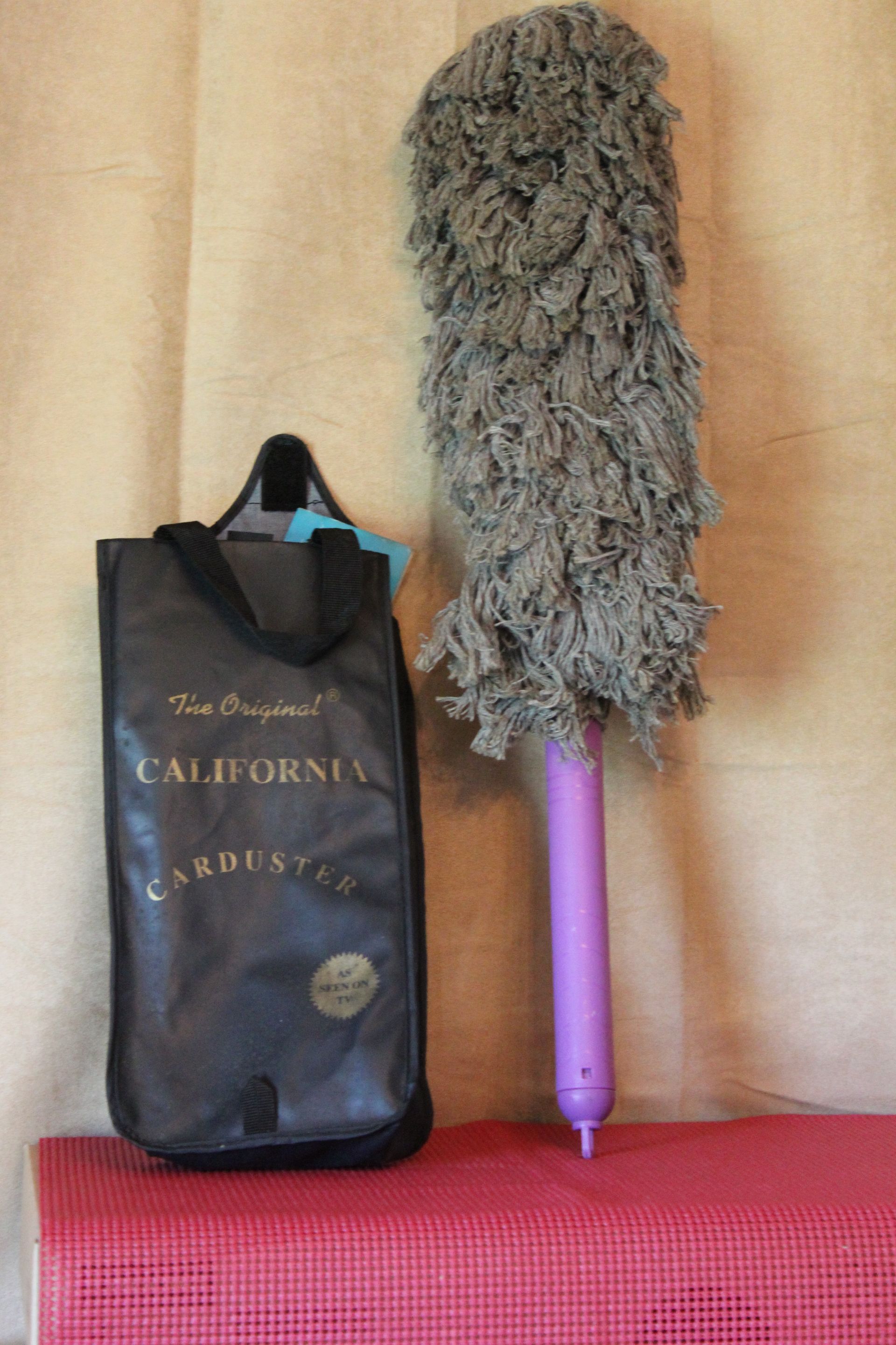 Purple hair straightener beside a black California bag on a beige wall and red surface
