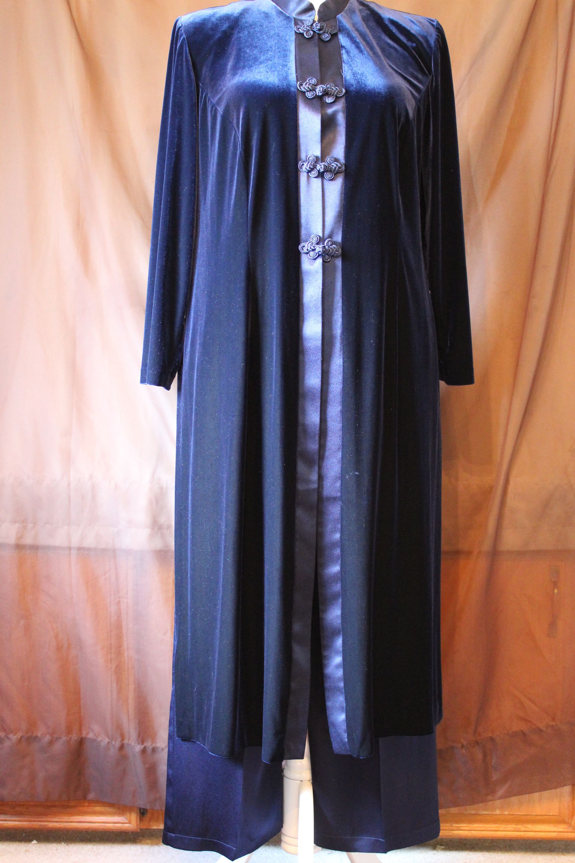 Blue long coat with black trim displayed on a mannequin against a tan curtain background