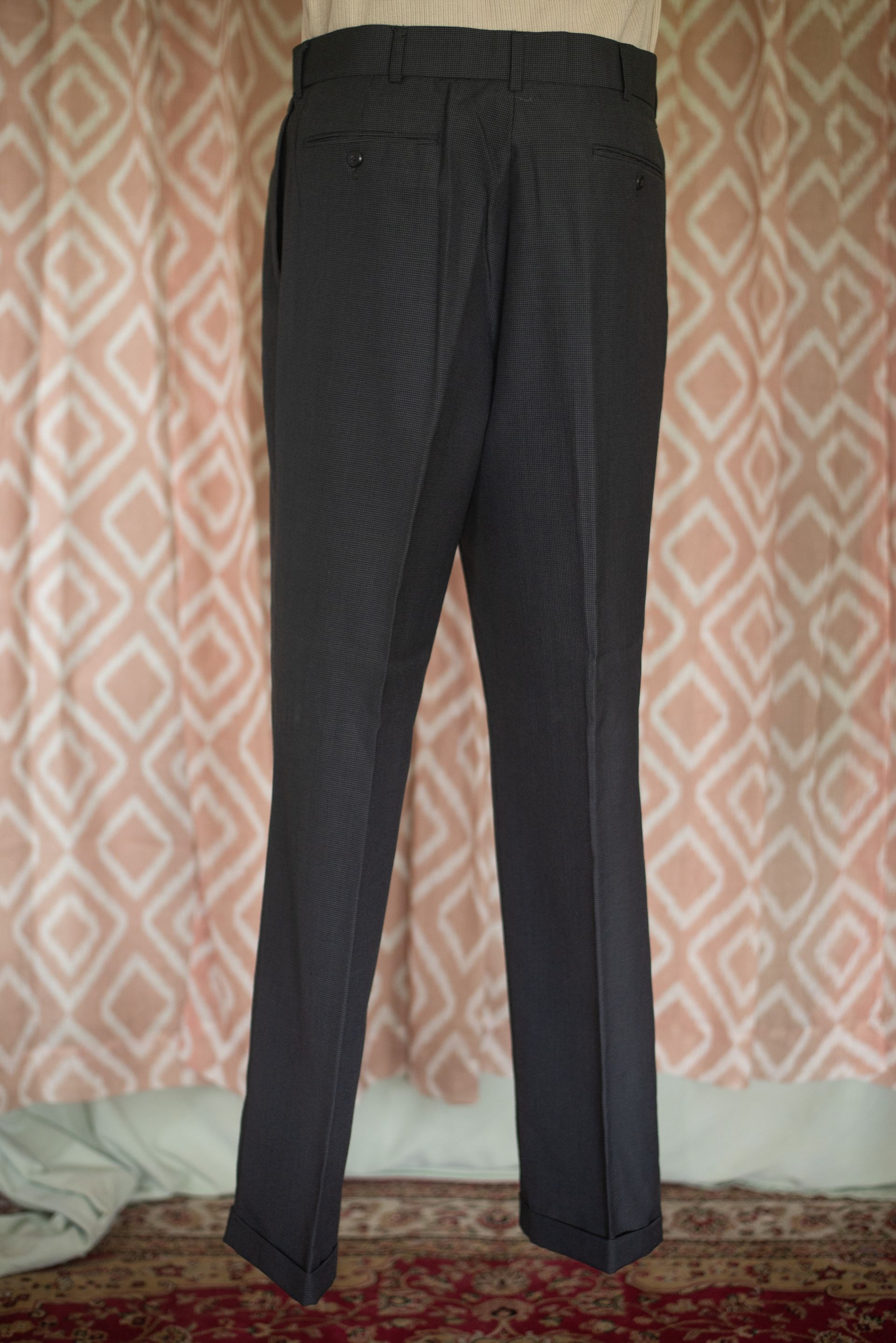 Dark striped trousers hanging against a patterned wall.