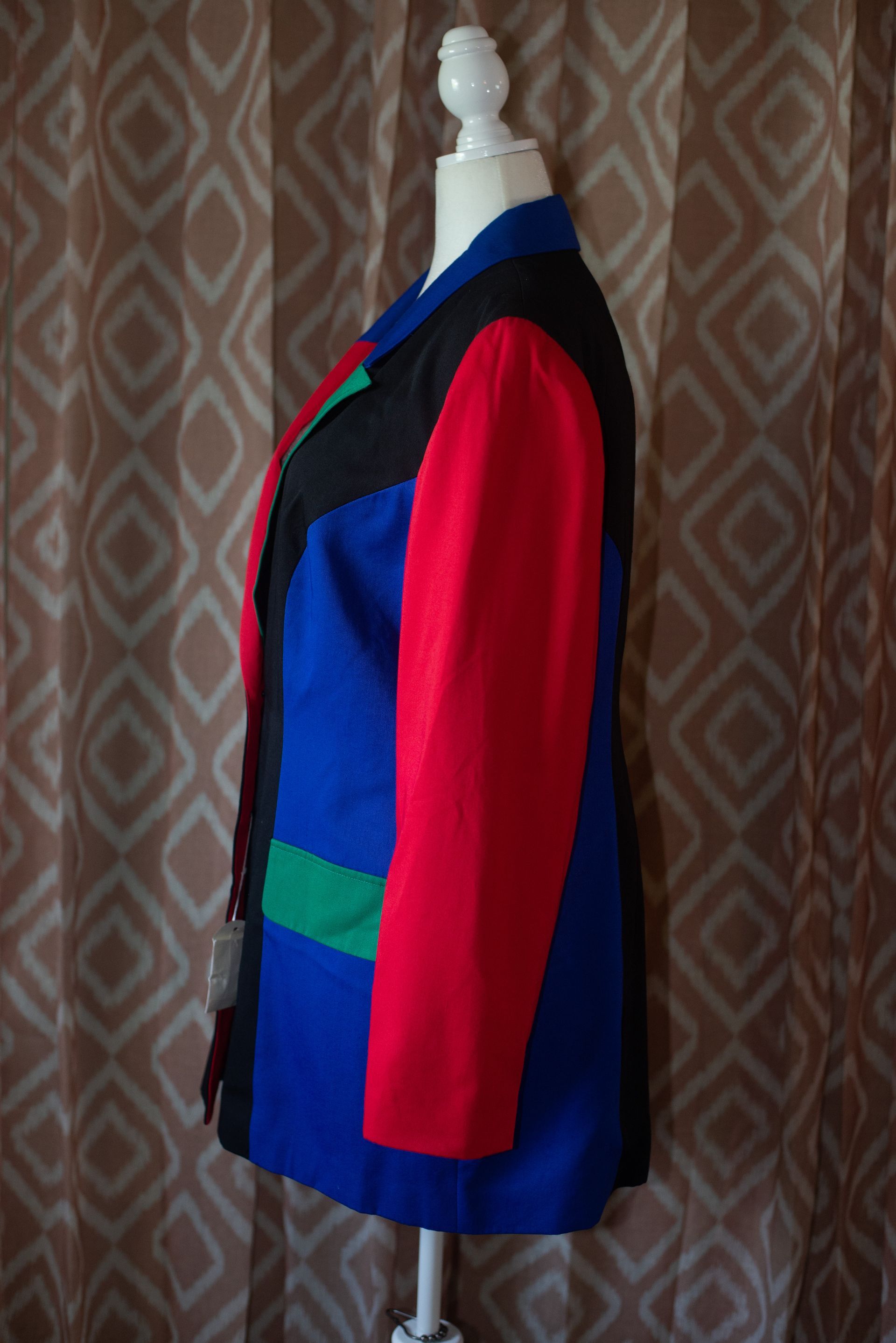 Colorful patchwork jacket with red sleeves on a mannequin against a patterned curtain background