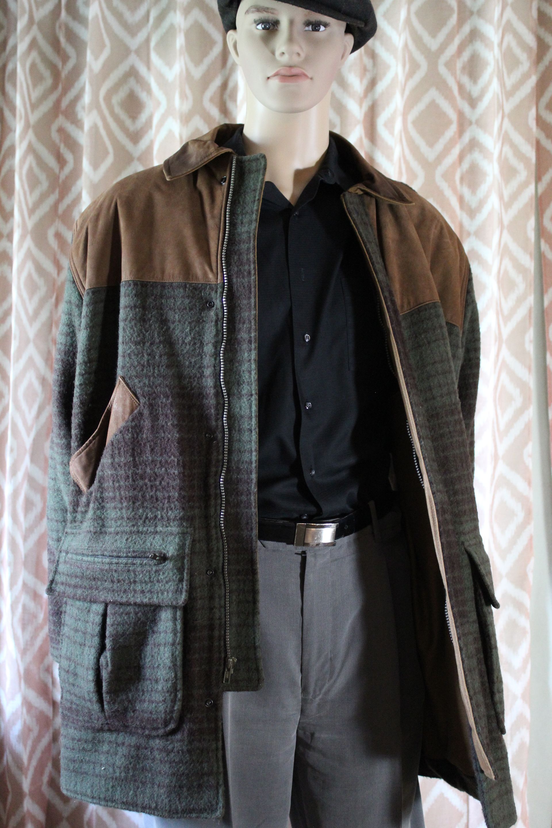 Mannequin wearing a beret, black shirt, and gray-brown coat in front of patterned curtains