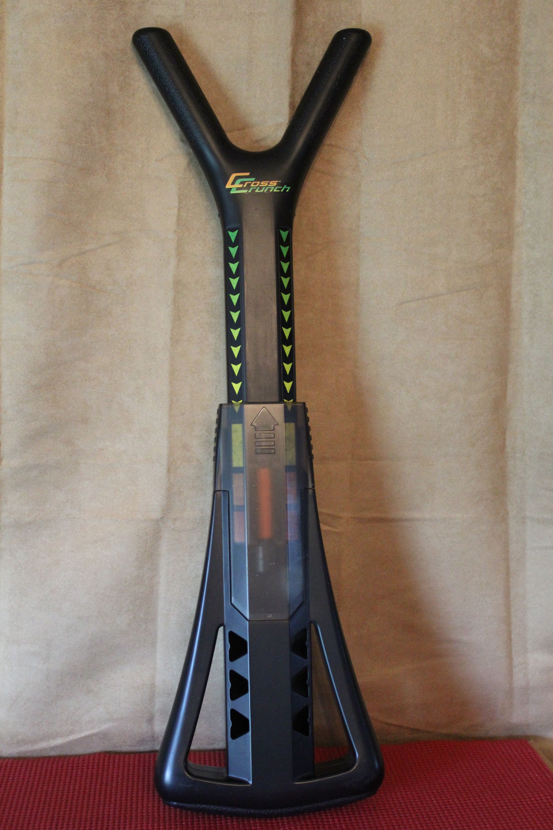 Y-shaped black and green sports launcher standing upright on a red surface against a beige wall