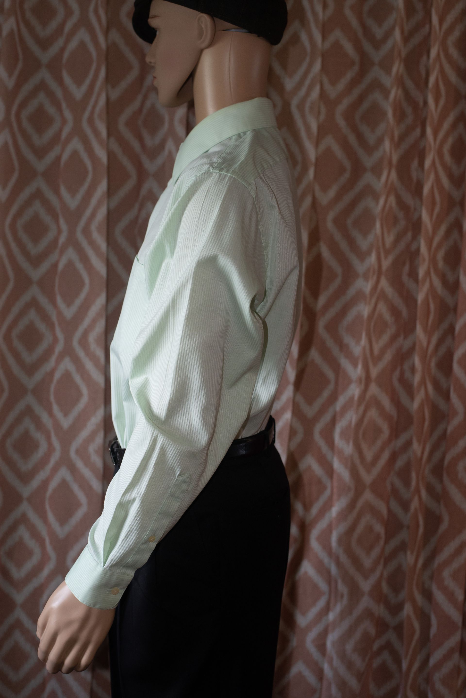 Mannequin in a white button-up shirt, black beret, and dark trousers against a patterned wallpaper backdrop