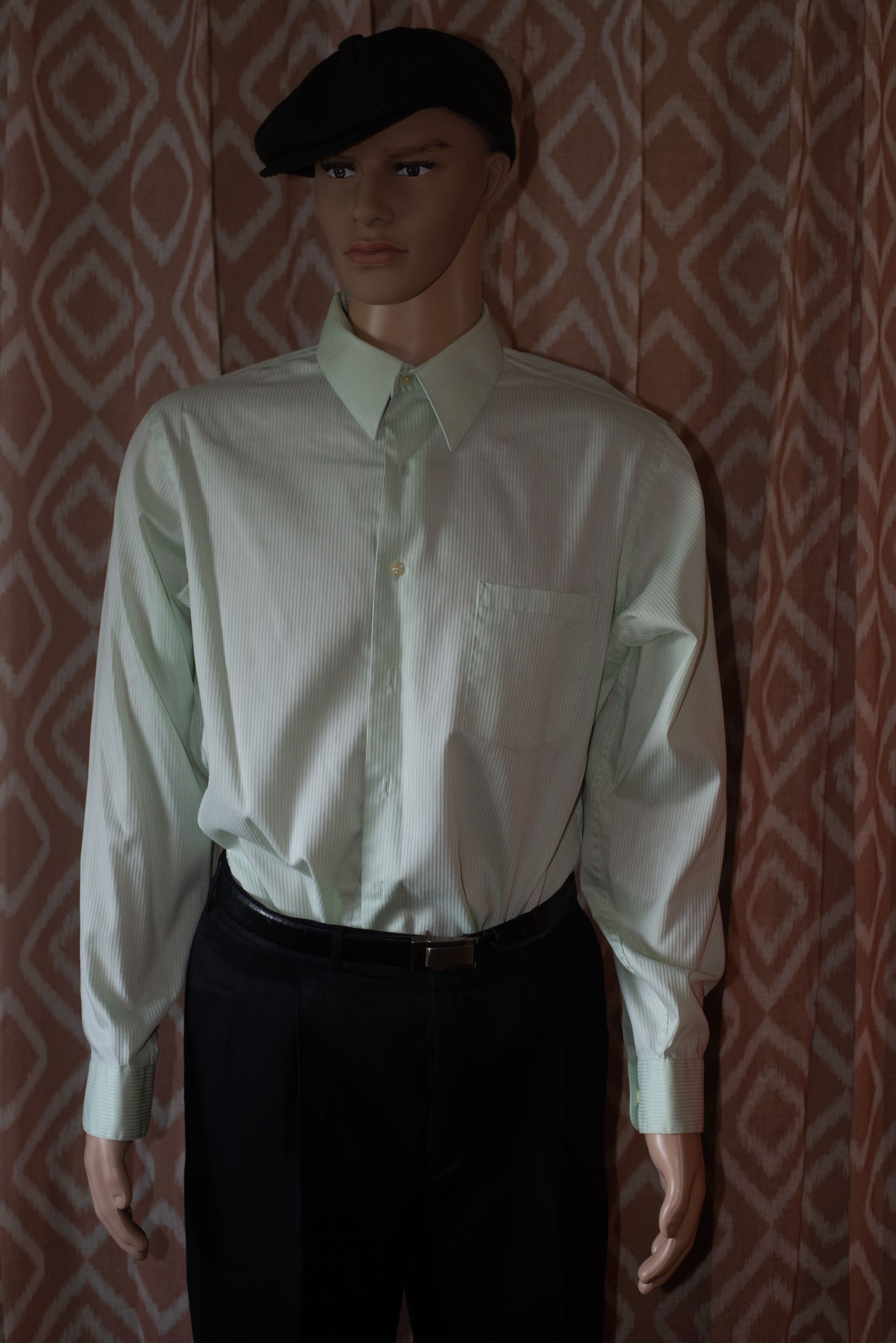 Mannequin in a white button-up shirt, black beret, and dark trousers against a patterned wallpaper backdrop