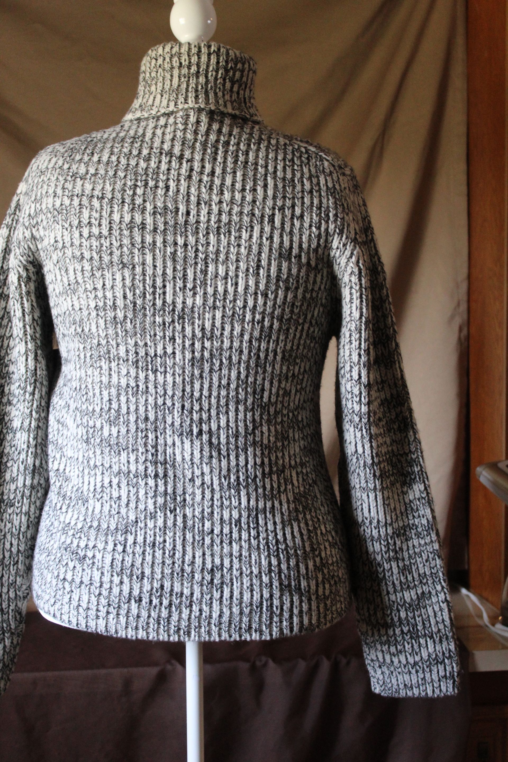 Gray knit turtleneck sweater displayed on a mannequin against a dark background.