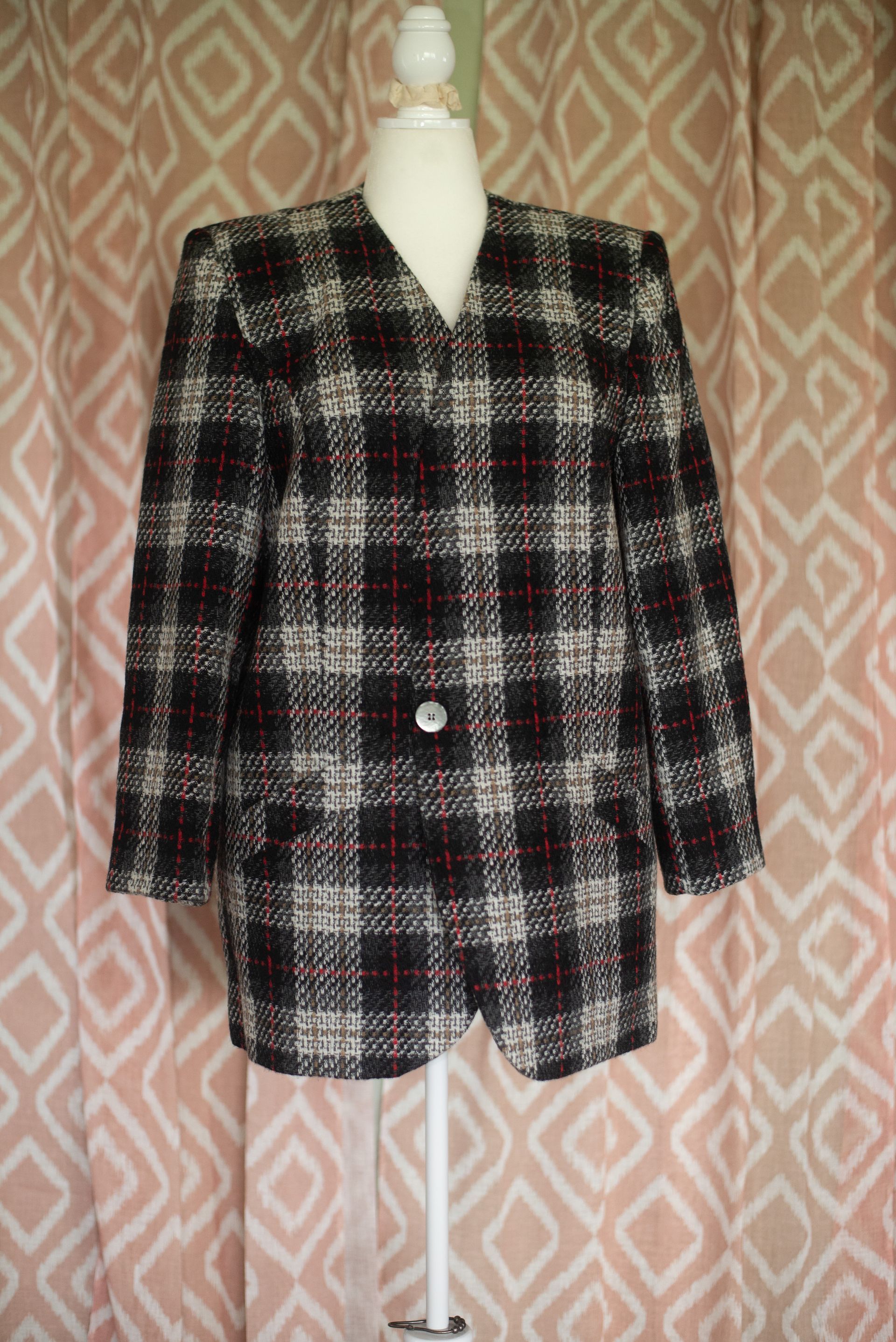 Plaid black, white, and red blazer on a mannequin against a pink patterned backdrop