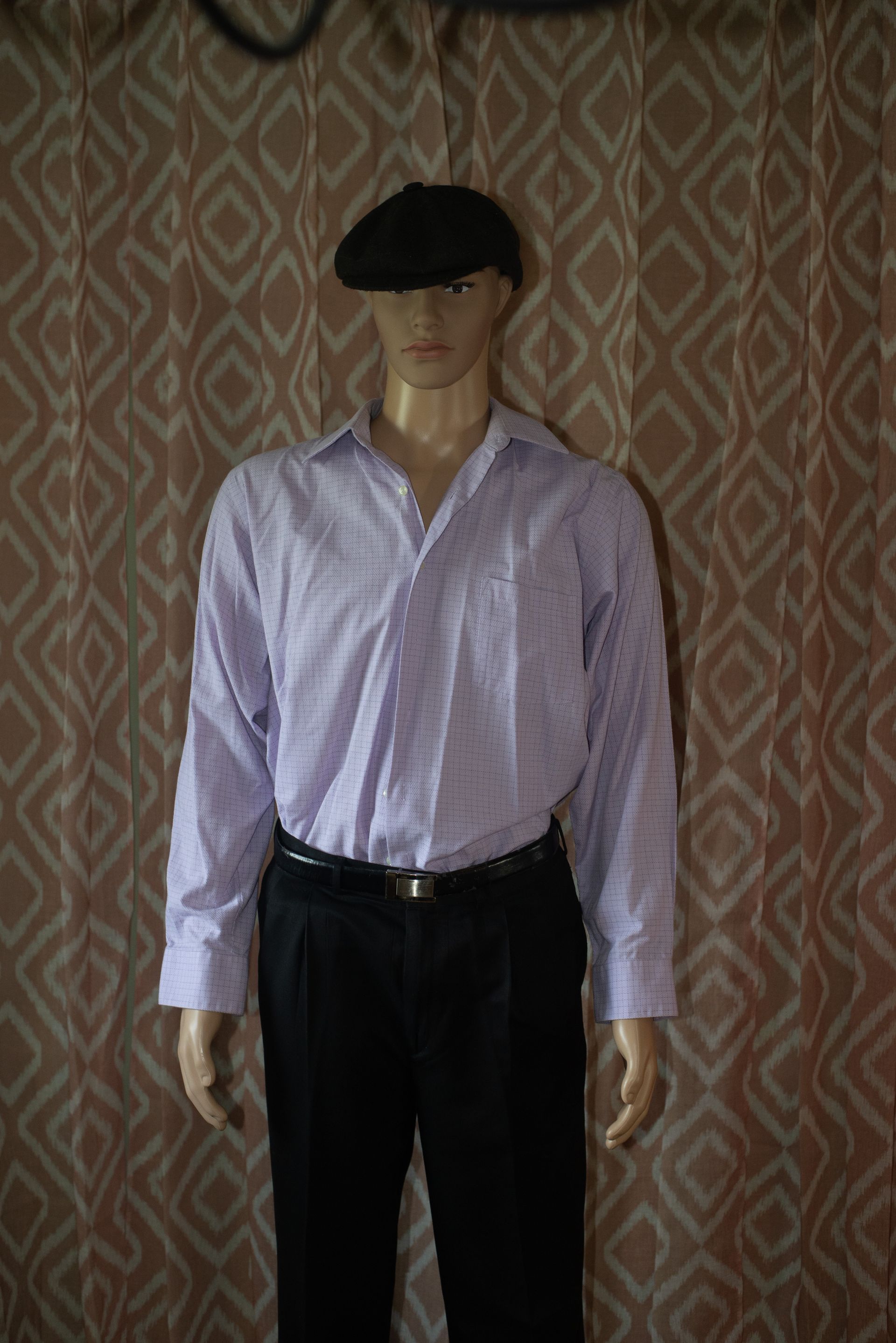 Mannequin in a light purple striped shirt, black pants, and black beret against a patterned backdrop