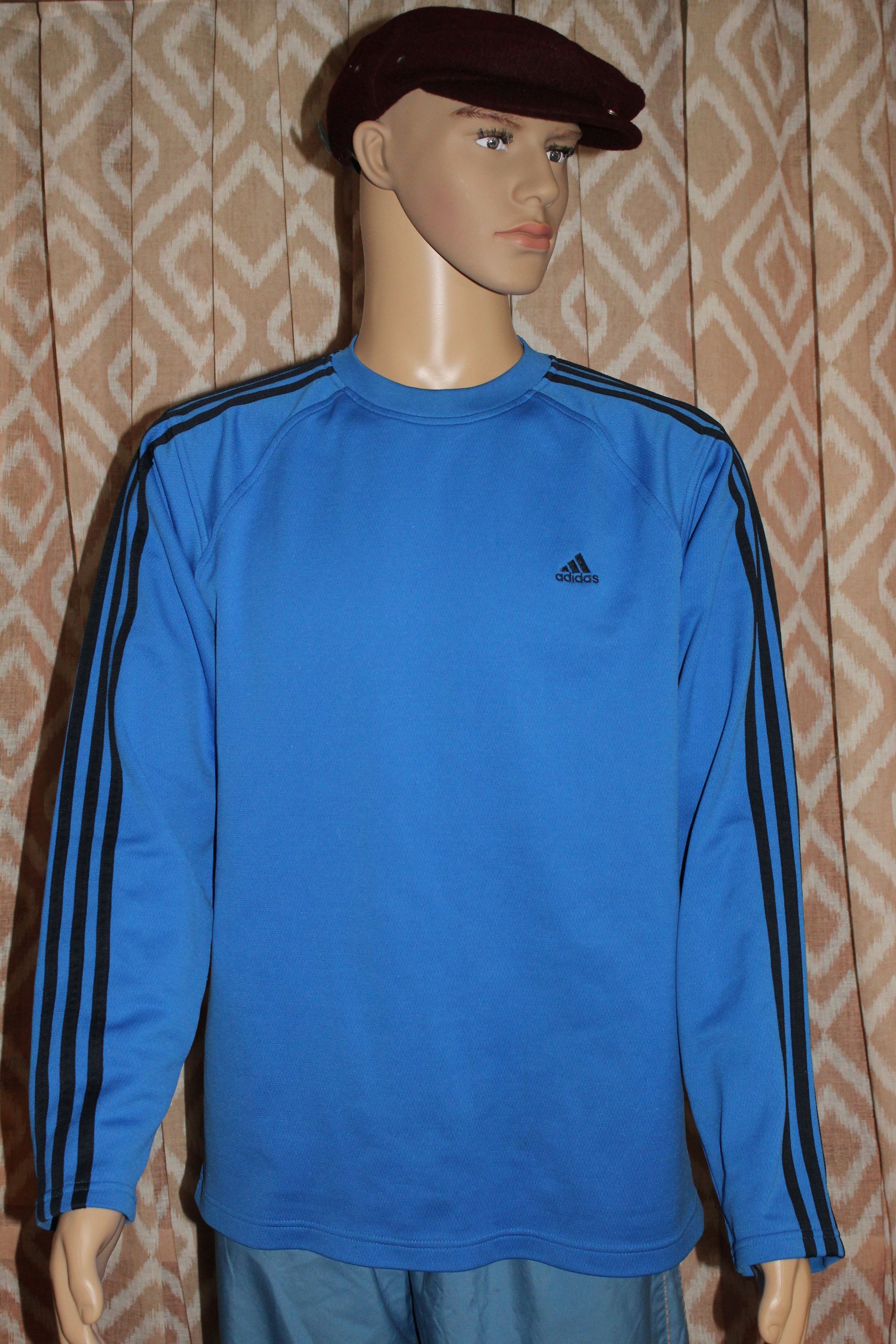 Mannequin wearing a blue long-sleeve shirt and brown cap against patterned wallpaper