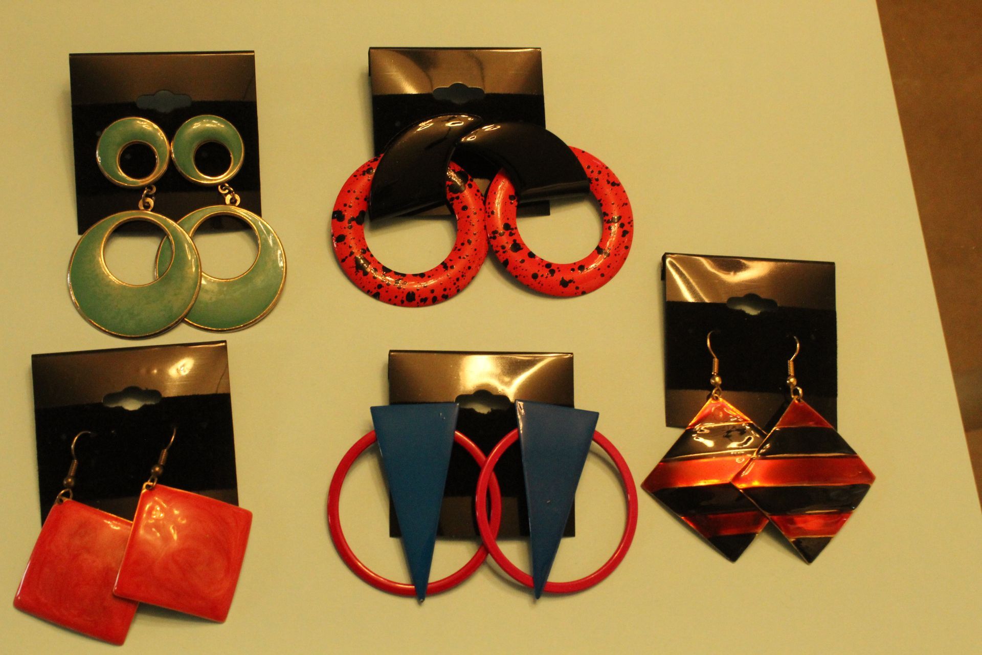 Assorted colorful earrings displayed on black cards against a beige background.