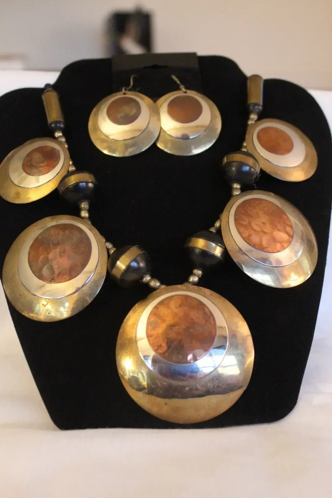 Gold and silver pendant necklace with oval amber-colored stones displayed on a black stand.