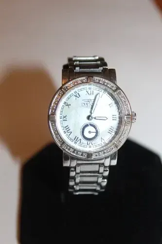 Diamond-encrusted silver wristwatch on a black stand against a light background
