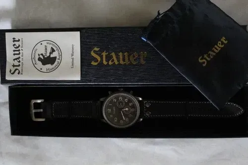 Stauer watch and black belt displayed in a box with gold logo and card