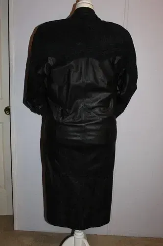 Black jacket and skirt on a mannequin, viewed from the back against a plain wall.