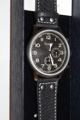 Stauer watch and black belt displayed in a box with gold logo and card