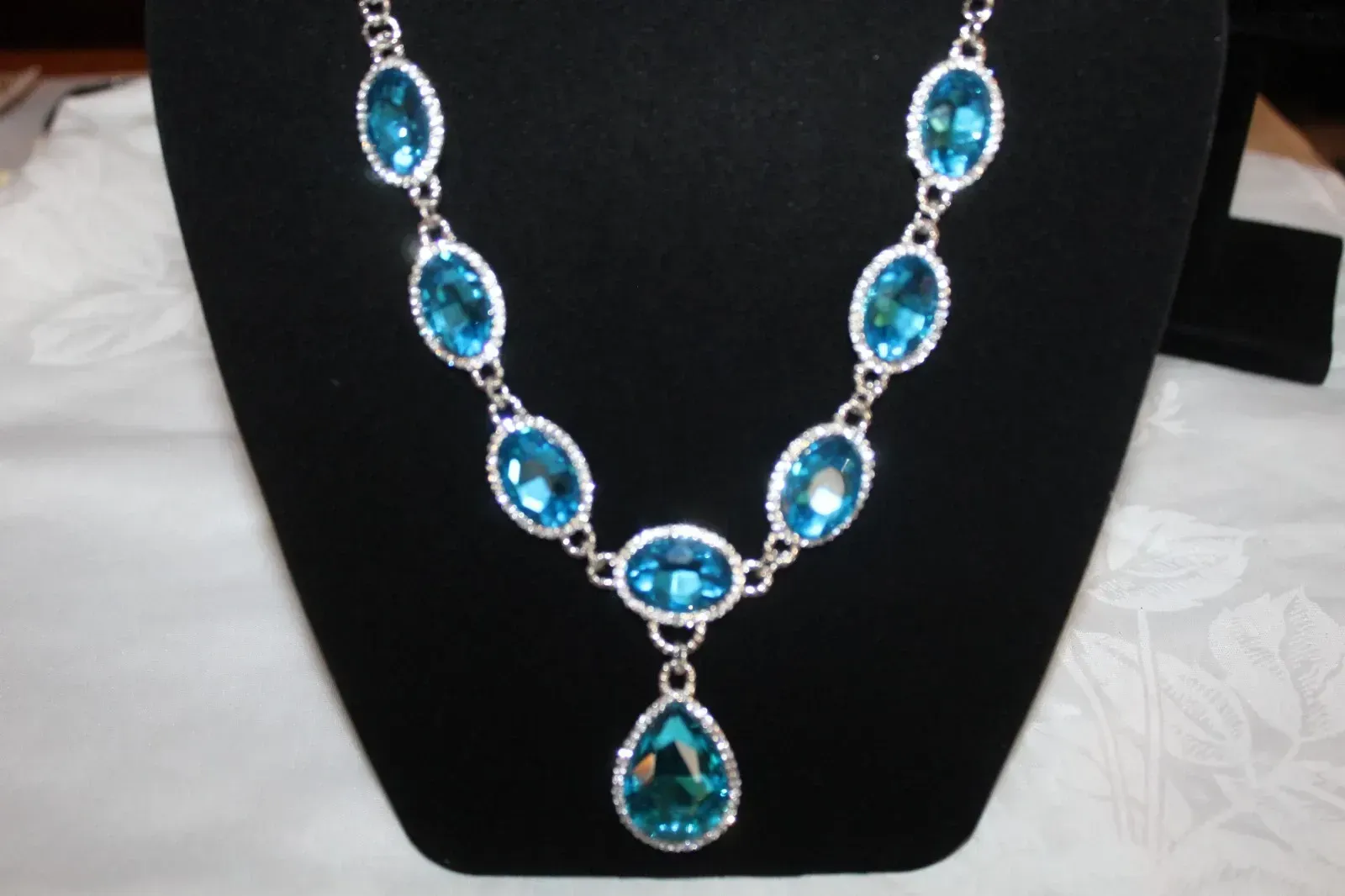 Blue gemstone necklace with silver settings displayed on a black velvet bust stand