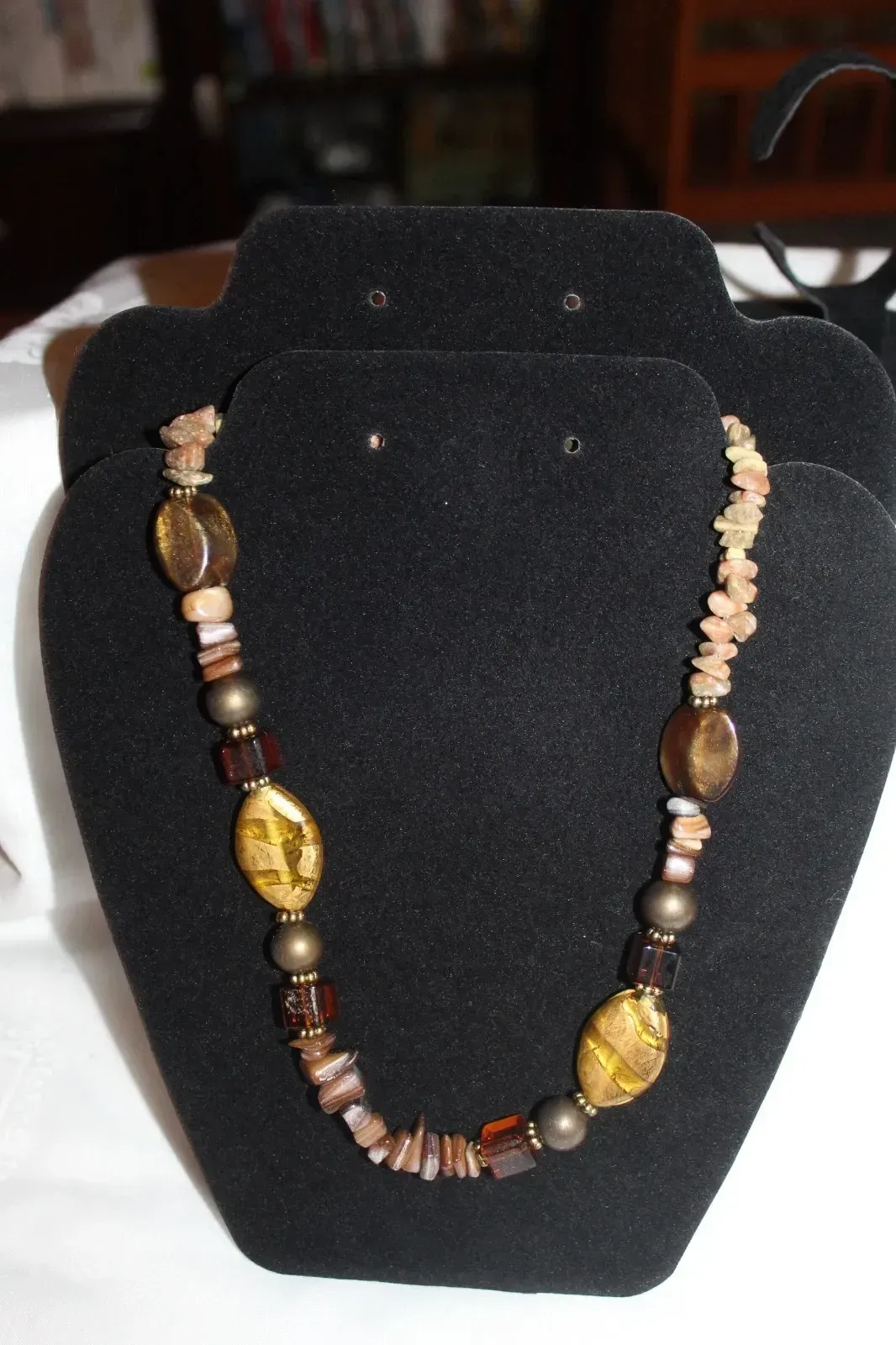 Beaded necklace with gold and brown accents displayed on a black jewelry stand.