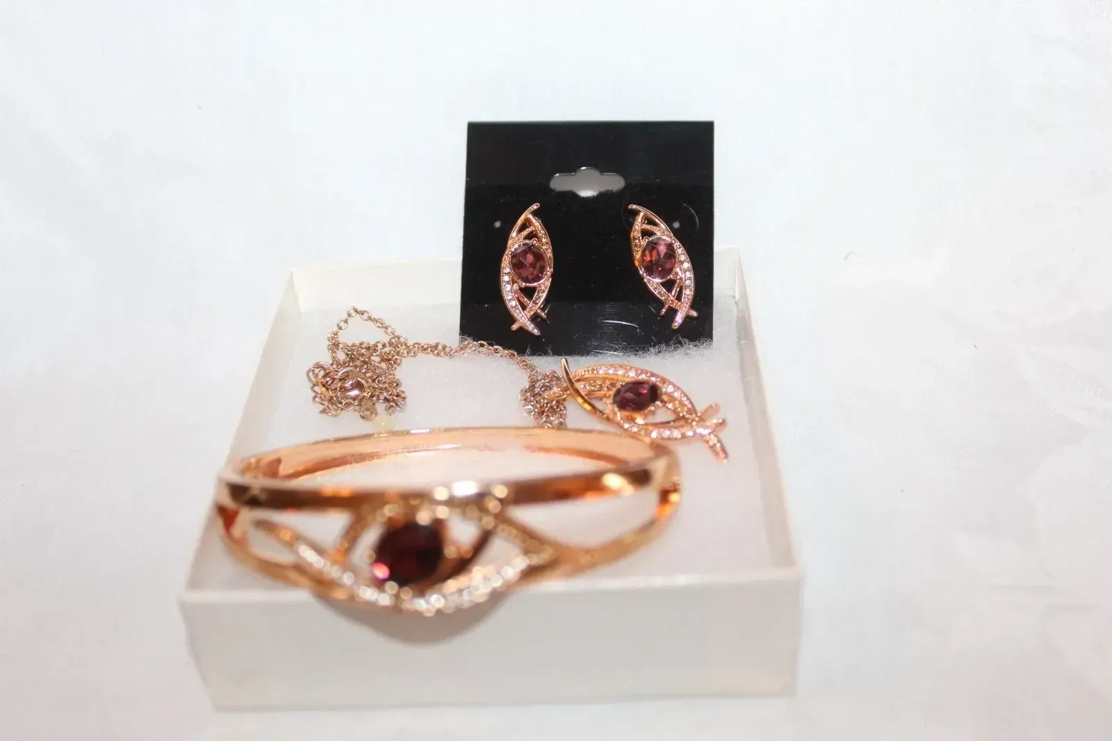 Rose gold jewelry set with bracelet, earrings, and ring displayed on a white tray