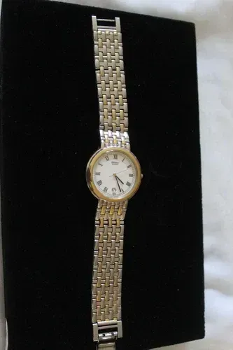 Gold and silver wristwatch on a black display stand with a white face and Roman numerals