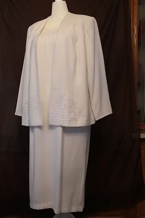 White ceremonial robe with wide sleeves and decorative hem, displayed on a mannequin against a dark background