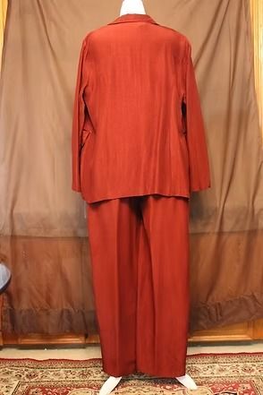 Red two-piece suit on a mannequin against a brown curtain background.