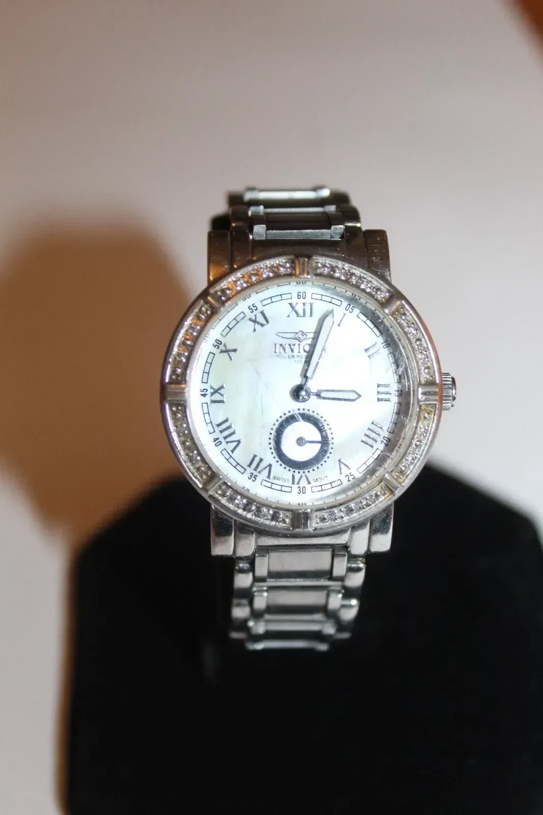 Diamond-encrusted silver wristwatch on a black stand against a light background