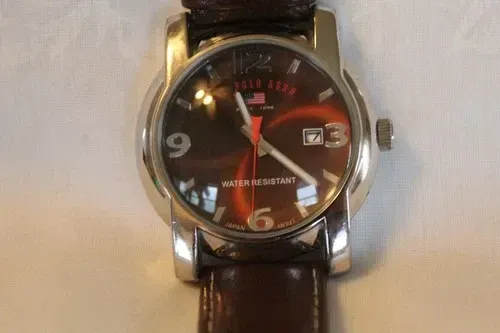 Close-up of a silver wristwatch with a brown leather strap and black dial on a light surface