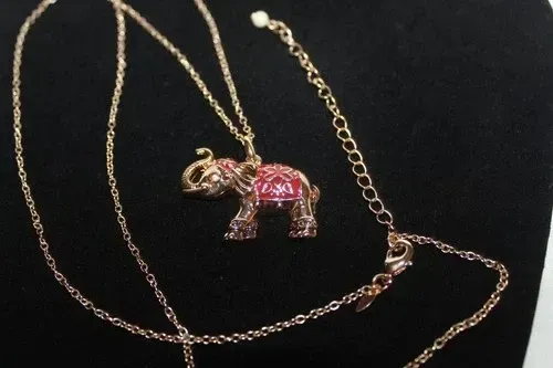 Gold necklace with a pink jeweled elephant pendant on a black background