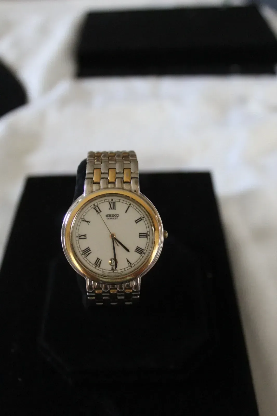 Gold and silver wristwatch on a black display stand with a white face and Roman numerals