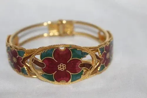 Gold bracelet with red and green floral enamel, flanked by matching fan-shaped earrings on a dark background
