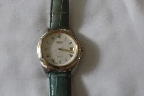 Gold watch with white face and green leather strap on a dark background
