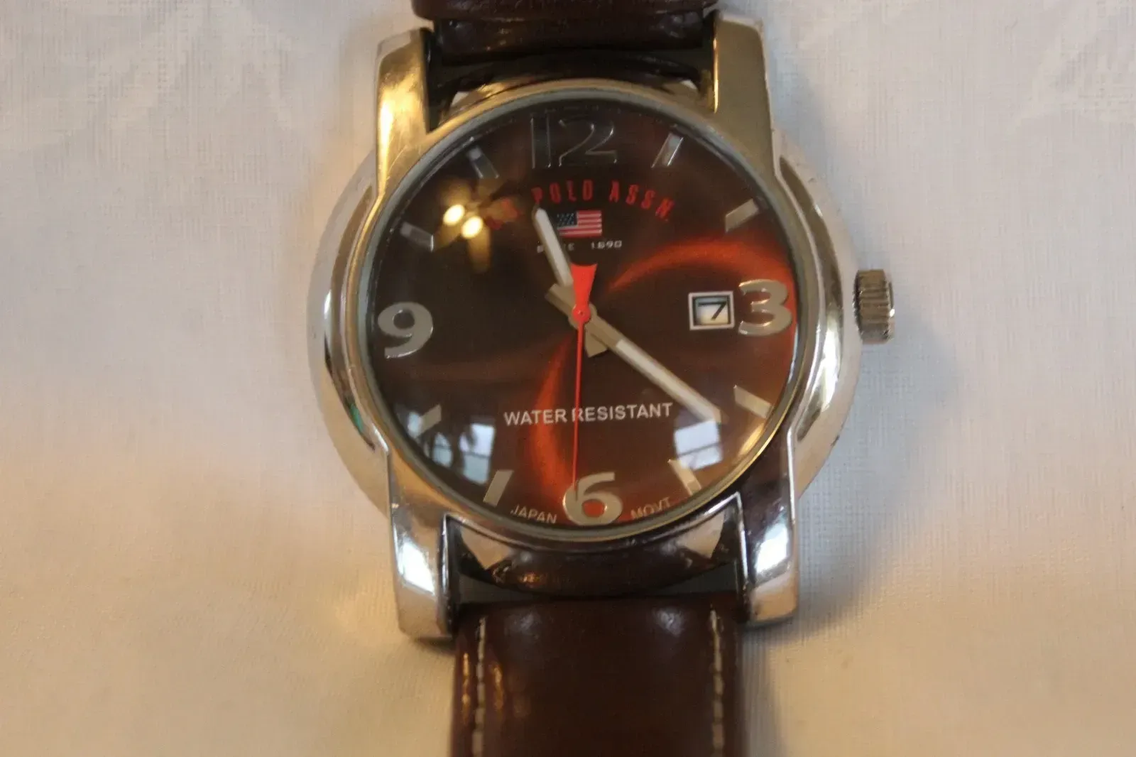 Close-up of a silver wristwatch with a brown leather strap and black dial on a light surface