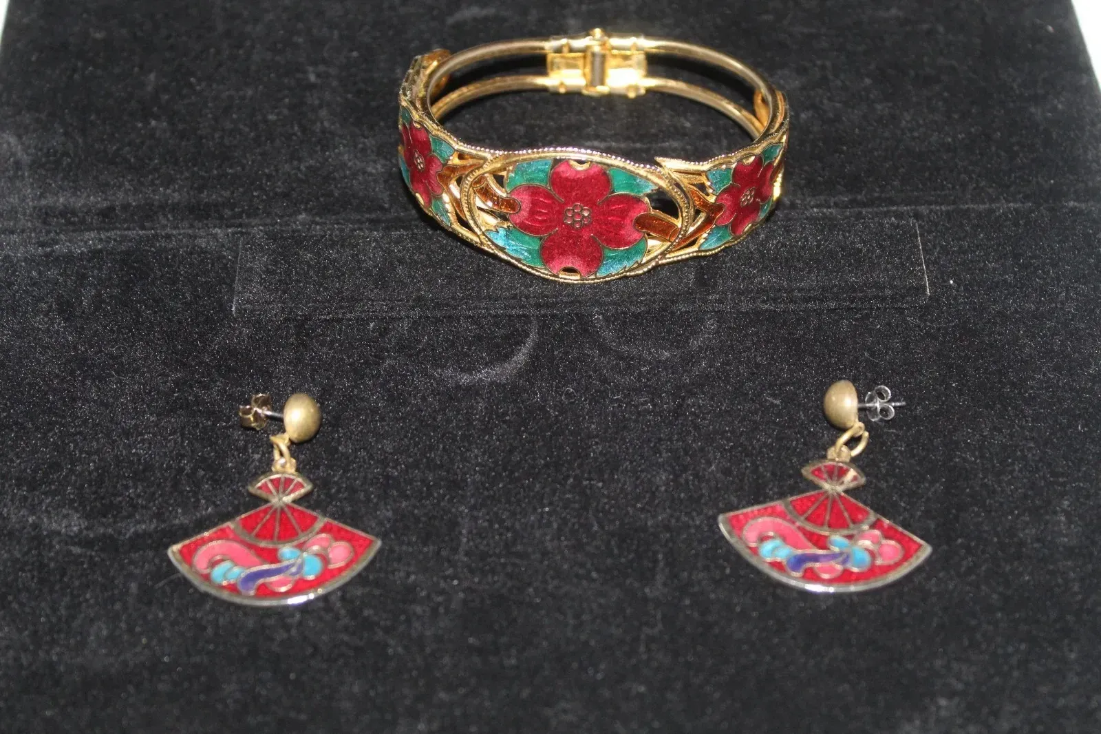 Gold bracelet and matching red-and-blue earrings with floral designs on a black background
