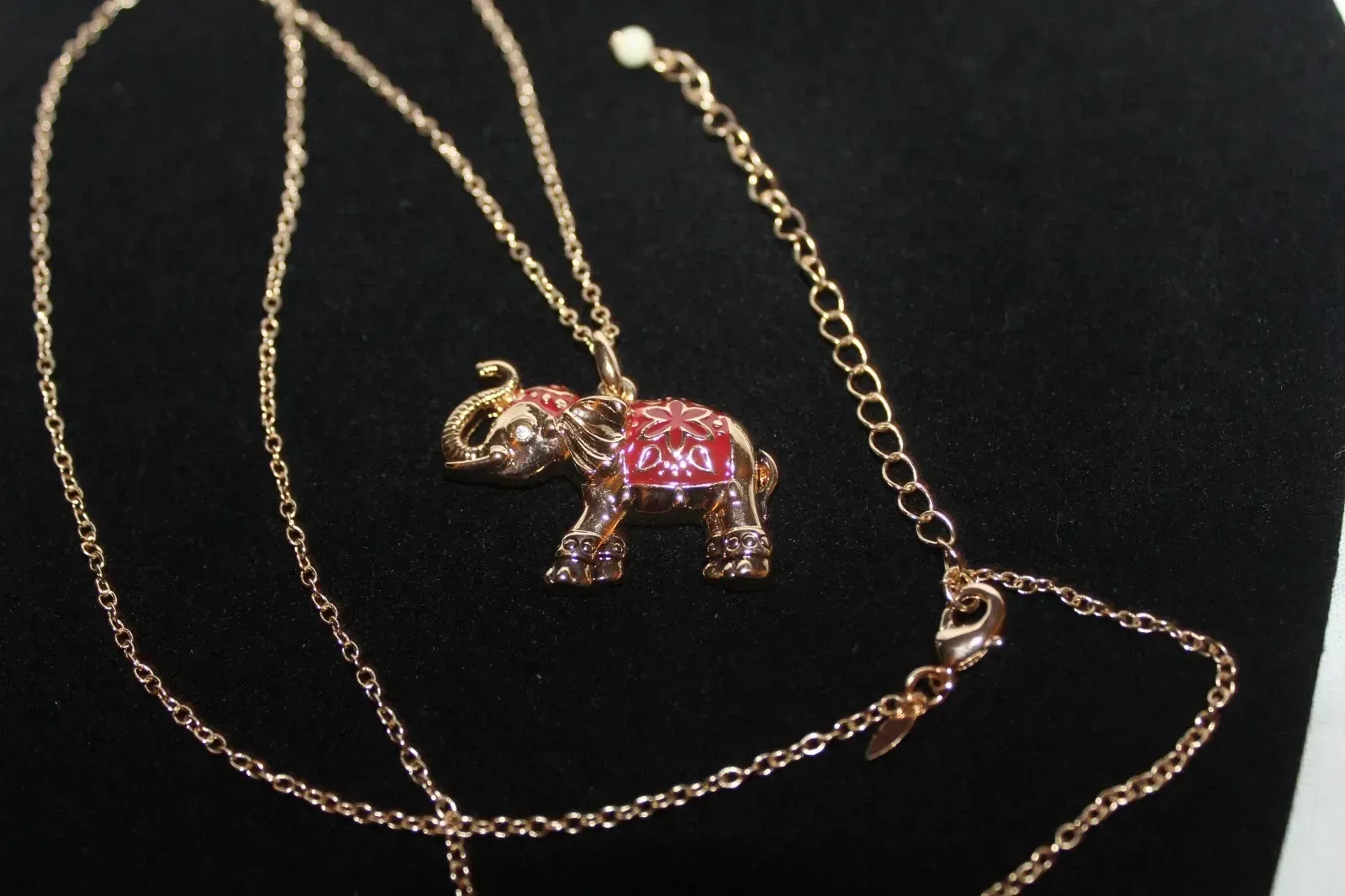 Gold necklace with a pink jeweled elephant pendant on a black background