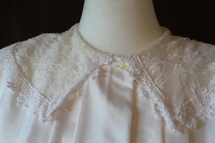 White lace-collared blouse with a small yellow flower clasp at the neckline