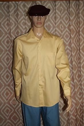 Mannequin in a yellow shirt, blue pants, and black hat standing before patterned curtains