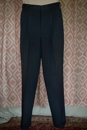 Dark navy trousers hanging against a patterned wall and carpeted floor.