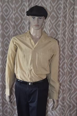 Mannequin wearing a tan shirt, black pants, and black cap against a patterned curtain backdrop
