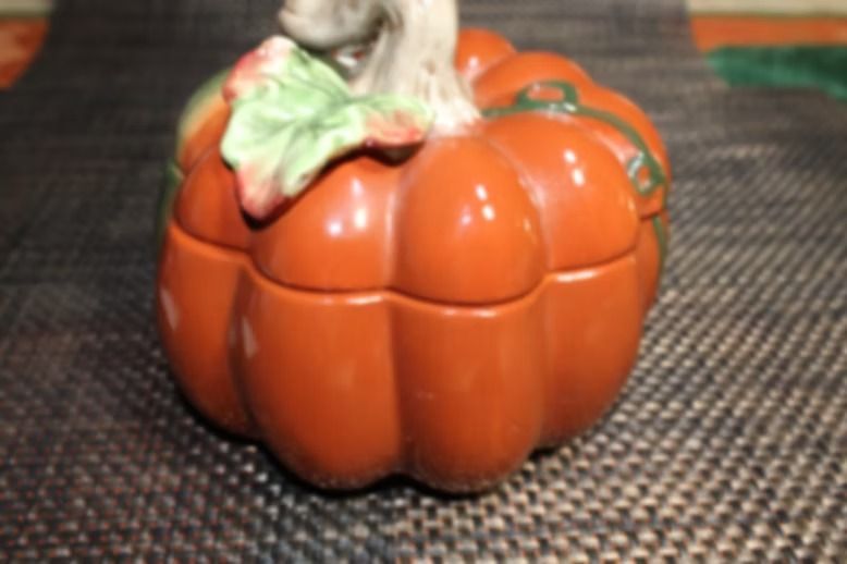 Orange pumpkin decoration on a woven mat, with a green stem and leaf detail