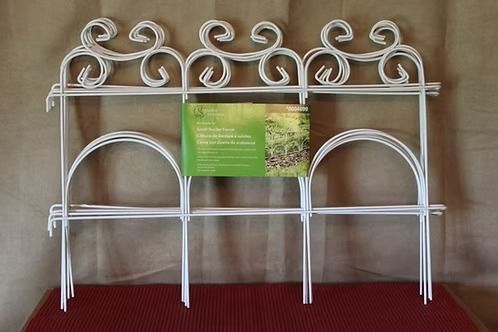 White decorative metal garden trellis with scrollwork, holding a green sign against a tan background.