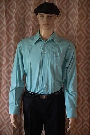 Mannequin wearing a teal button-down shirt, black pants, and black cap against a patterned curtain background