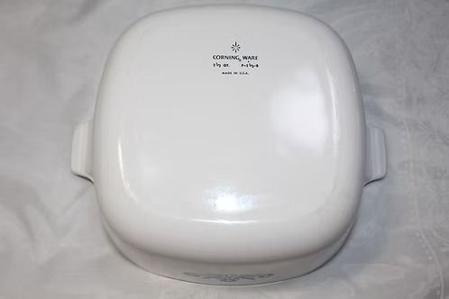 White countertop kitchen appliance with a glossy lid and side handles on a fabric surface