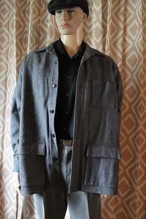 Mannequin wearing a gray jacket, black shirt, and cap in front of patterned curtains