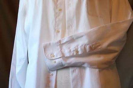Close-up of a white dress shirt sleeve being rolled up by a hand