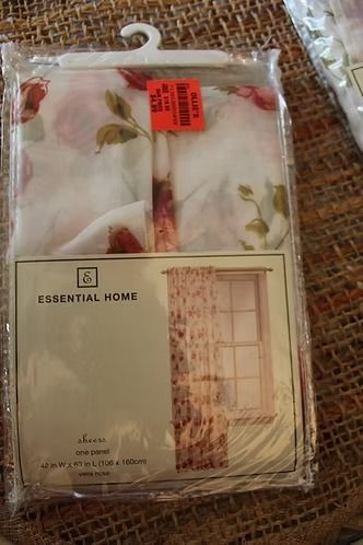 Packaged floral sheer curtains with beige window and chair illustration, hanging on a white hook with red sale sticker