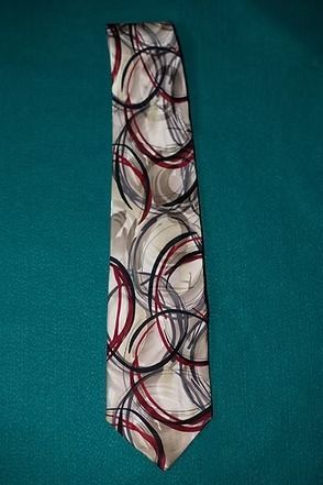 White necktie with red, black, and gray circular pattern on a teal background